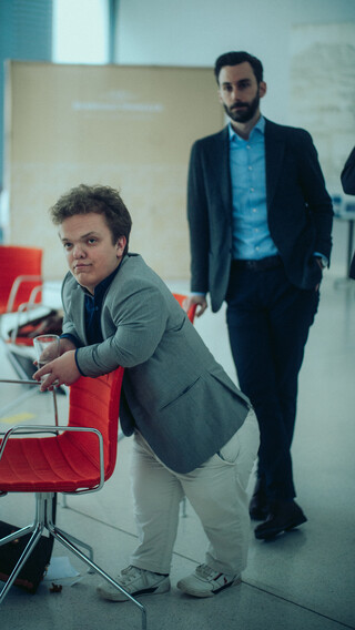 Zwei Herren in Geschäftskleidung posieren mit Sesseln.