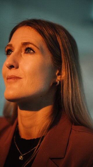 Dame mit blonden, langen Haaren im Portrait. Sie wird von vorne von einem warmen Licht angestrahlt.