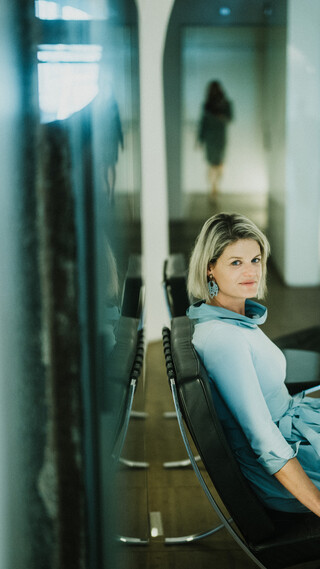 Eine Dame in Kleid sitzt lächelnd auf der Bank eines modernen Gaa