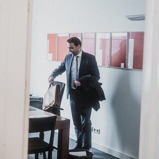 Ein Mann im blauen Anzug nimmt seine Tasche vom Stuhl.