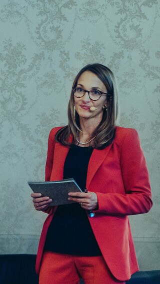 Eine Dame in Geschäftskleidung ist mit Headset und Moderationskarten ausgerüstet.