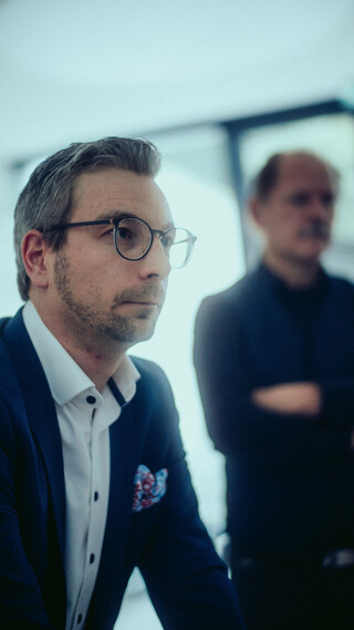 Zwei Herren in Geschäftskleidung blicken in die gleiche Richtung.