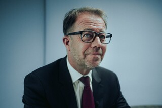 Ein Herr in Anzug sitzt lächelnd an einem Tisch.