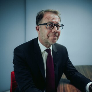 Ein Herr in Anzug sitzt lächelnd an einem Tisch.