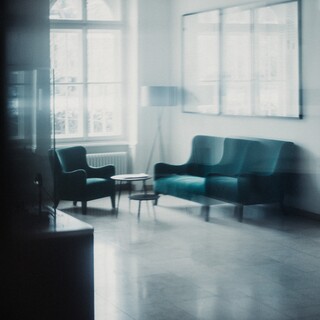 In einem Wohnraum befinden sich 2 kleine Tische, 2 Sessel und eine weiße Stehlampe.