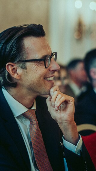 Lächelnde Herren in Anzügen blicken in die gleiche Richtung.