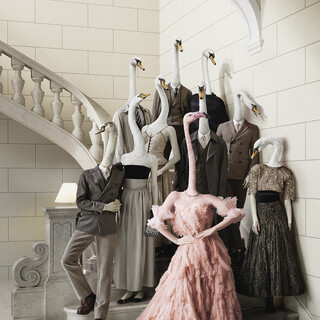 Webesujet des Bankhaus Spängler: Eine dunkel-gekleidete Familie mit Schwan-Köpfen steht auf einer Treppe. Eine Dame sticht besonders hervor - sie hat einen Flamingo-Kopf und trägt ein opulentes Kleid in rosa Farbe.