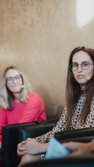 Drei Damen und ein Herr in Geschäftskleidung mit Headset während einer Podiumsdiskussion.