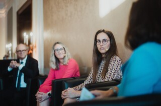 Drei Damen und ein Herr in Geschäftskleidung mit Headset während einer Podiumsdiskussion.