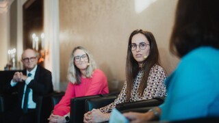 Drei Damen und ein Herr in Geschäftskleidung mit Headset während einer Podiumsdiskussion.