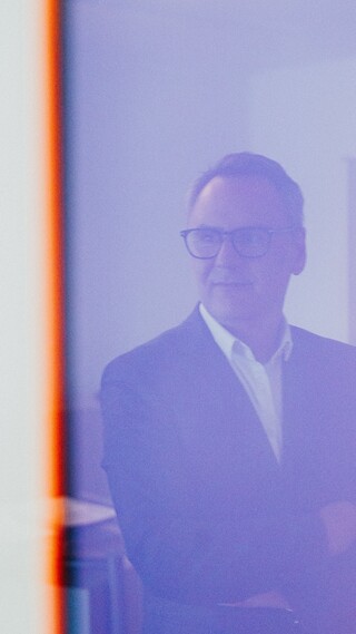 Ein lächelnder Herr in Geschäftskleidung spiegelt sich in einem Gemälde.