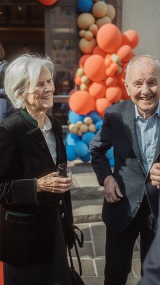 Drei Personen in Geschäftskleidung im Gespräch vor einem Gebilde aus Luftballons.