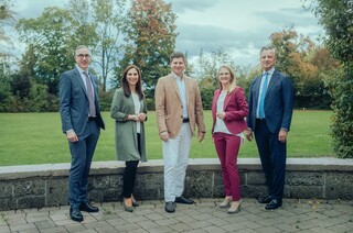 Dr. Werner Zenz (r.) steht draußen mit vier weiteren Personen in Anzügen, während im Hintergrund eine Wiese und Bäume zu sehen sind.