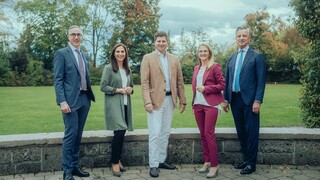 Dr. Werner Zenz (r.) steht draußen mit vier weiteren Personen in Anzügen, während im Hintergrund eine Wiese und Bäume zu sehen sind.