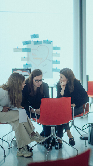 Drei Damen sitzen in einem modernen Saal in einer Reihe und kommunizieren miteinander.
