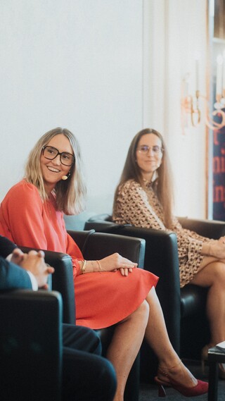 Drei Damen und ein Herr in Geschäftskleidung mit Headset während einer Podiumsdiskussion.