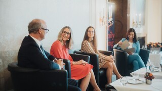 Drei Damen und ein Herr in Geschäftskleidung mit Headset während einer Podiumsdiskussion.