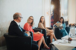 Drei Damen und ein Herr in Geschäftskleidung mit Headset während einer Podiumsdiskussion.