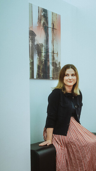 Eine lächelnde Dame in Geschäftskleidung sitzt auf einer Bank.