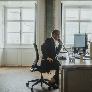 Ein Herr in Anzug telefoniert an einem Schreibtisch in einem historischen Büro.