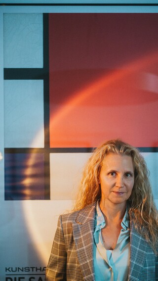 Eine Dame in Geschäftskleidung posiert vor einem Gemälde.