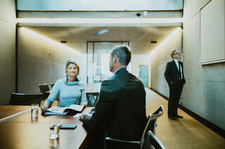 Drei Personen in Geschäftskleidung befinden sich in einem modernen Besprechungszimmer.