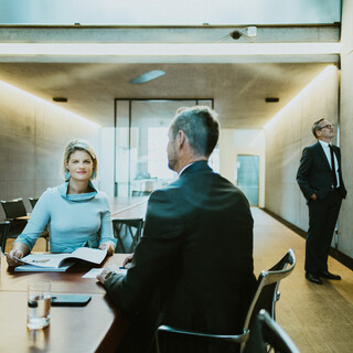 Drei Personen in Geschäftskleidung befinden sich in einem modernen Besprechungszimmer.