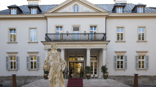 Historisches Gebäude "Kavalierhaus Klessheim" in Salzburg von außen. 3-stöckiges Gebäude mit Treppenaufgang und Statue vor Eingang.