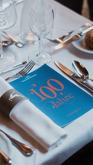 Ein festlich gedeckter Tisch mit einem Flyer "100 Jahre".
