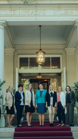 Elegant gekleidete Damen stehen lächelnd im Eingangsbereich eines historischen Gebäudes.