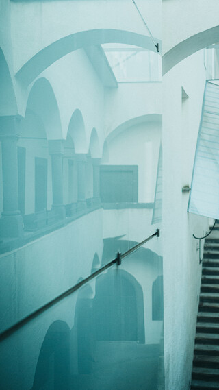 Ein düsterer Innenhof mit Arkaden spiegelt sich in einer Glaswand.