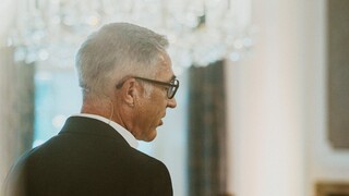 Vortragender in Anzug auf einer Bühne in einem historischen Saal.