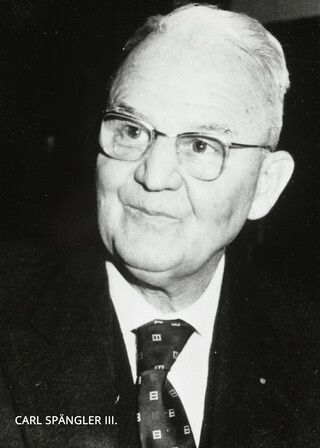Schwarz-weißes Portraitfoto von einem älteren Herren mit vermutlich grauen Haaren und eine Brille. Er trägt ein Sakko, Hemd und Krawatte. Ein Text ist vermerkt mit "Carl Spängler III."