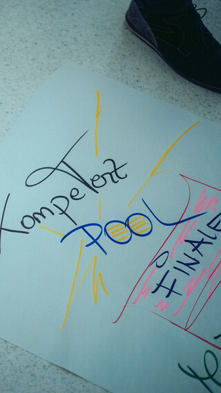 Zwei Personen stehen neben einem beschriebenen Plakat auf dem Boden.