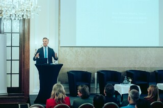 Dr. Werner Zenz hält eine Rede vor dem Publikum im Rahmen des Forums Familienunternehmen 2024. In der linken oberen Ecke ist ein Kronleuchter zu sehen, im rechten Teil des Bildes eine Leinwand. 