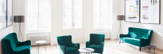 Helle Büroräumlichkeiten des Bankhaus Spängler mit mehreren grünen Sitzgelegenheiten sowie Tischen und Lampen sind ersichtlich. 