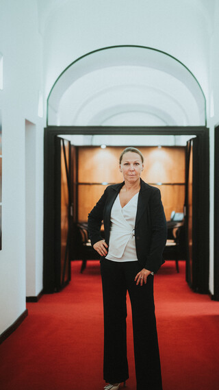 Eine Dame in Geschäftskleidung steht in einem Gang mit rotem Teppich.