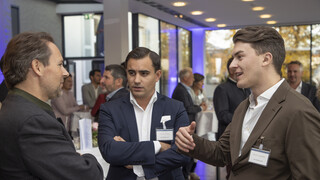 Drei Männer sprechen miteinander und befinden sich in einem Veranstaltungsraum.