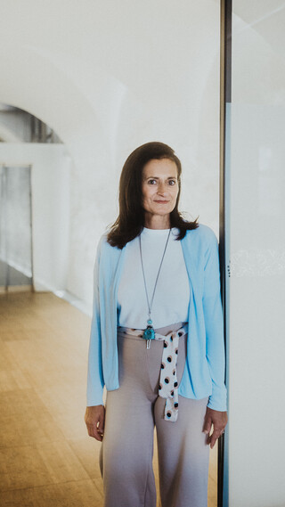 Eine Dame lehnt lächelnd an einer Glaswand in einem modernen Raum.