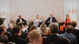 Elegant gekleidetes Publikum lauscht einer Podiumsdiskussion.