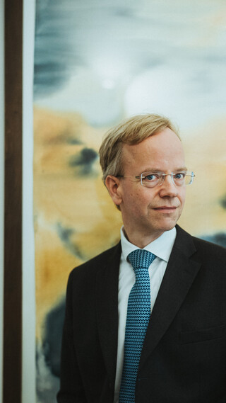 Ein Herr mit einem skeptischen Blick posiert vor einem Gemälde.