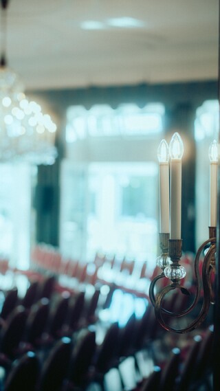 Leere Zuschauerränge unter einem Kronleuchter in einem historischen Raum.