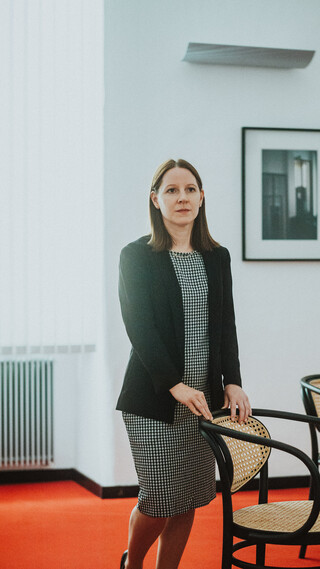 Eine Dame in Geschäftskleidung hält die Lehne eines Sessels.