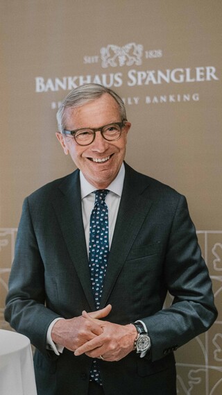 Ein lächelnder Herr in Geschäftskleidung steht an einem Stehtisch.