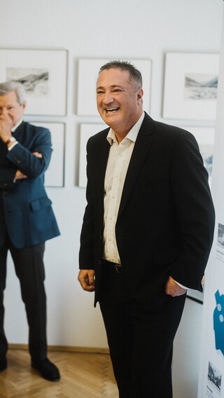 Ein lächelnder Herr in Anzug und ein weiterer in nachdenklicher Pose.