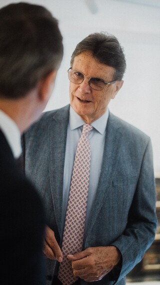 Ein älterer Herr in Anzug führt ein Gespräch mit einem anderen Herren.