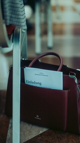 Eine Handtasche steht neben einem Sessel auf dem Boden.