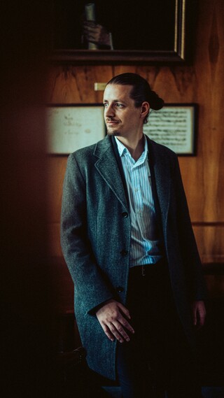 In einem dunklen Raum sitzt ein Mann und schaut nach rechts.