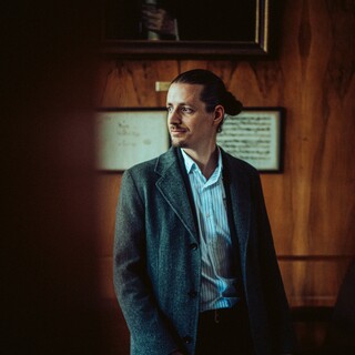 In einem dunklen Raum sitzt ein Mann und schaut nach rechts.