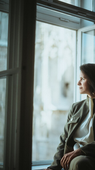 Eine Dame in Geschäftskleidung sitzt auf einer Fensterbank und blickt nach draußen.